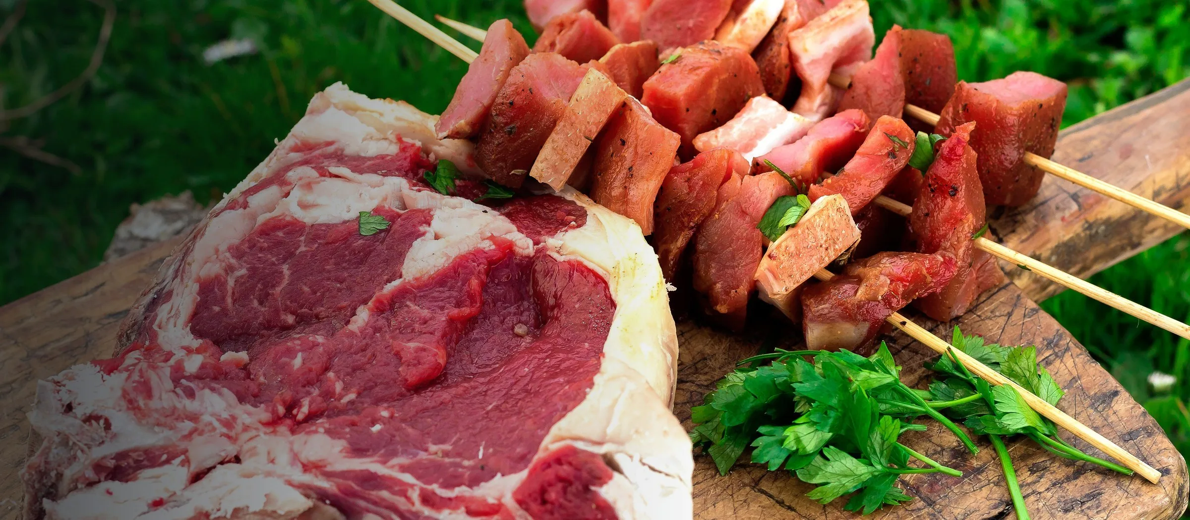 Raw cuts of red meat and seasoned skewers on a wooden board