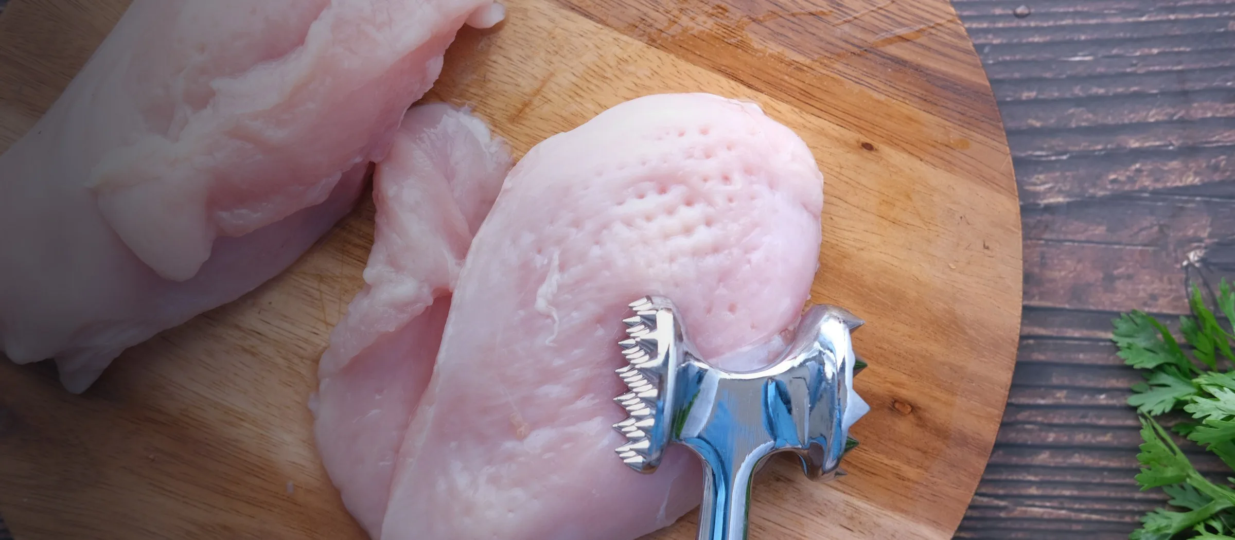 Raw chicken breasts on a wooden board with a meat tenderiser